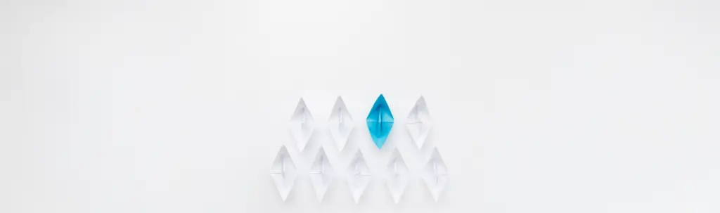 A conceptual image for business leadership featuring a fleet of white origami paper boats following a single bright blue paper boat, symbolizing guidance, strategy, and standing out in the workplace.